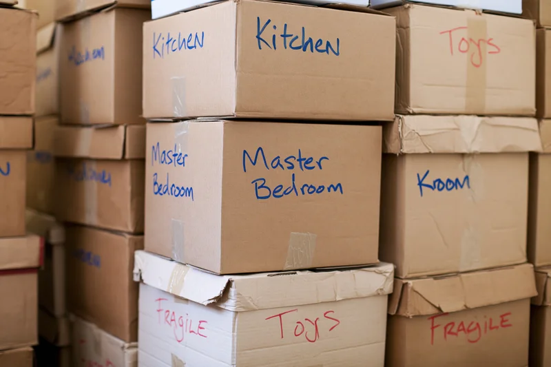 Stacked cardboard moving boxes labeled with room names and fragile warnings filling a storage space
