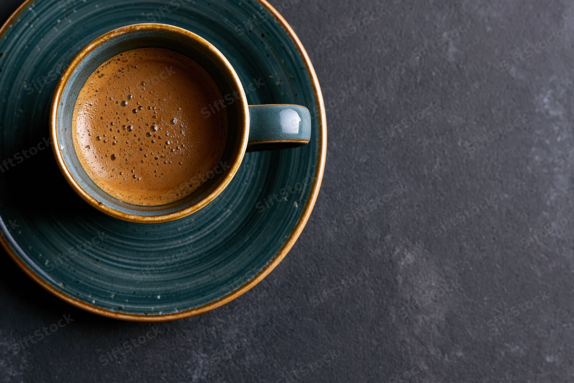 Teal ceramic espresso cup with foamy crema on dark surface, overhead view