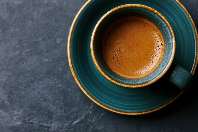 Overhead view of a teal ceramic espresso cup with crema on a dark stone surface