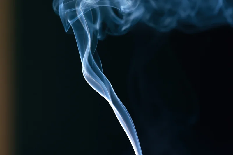 Thin wisp of white-grey smoke curling upward against dark background