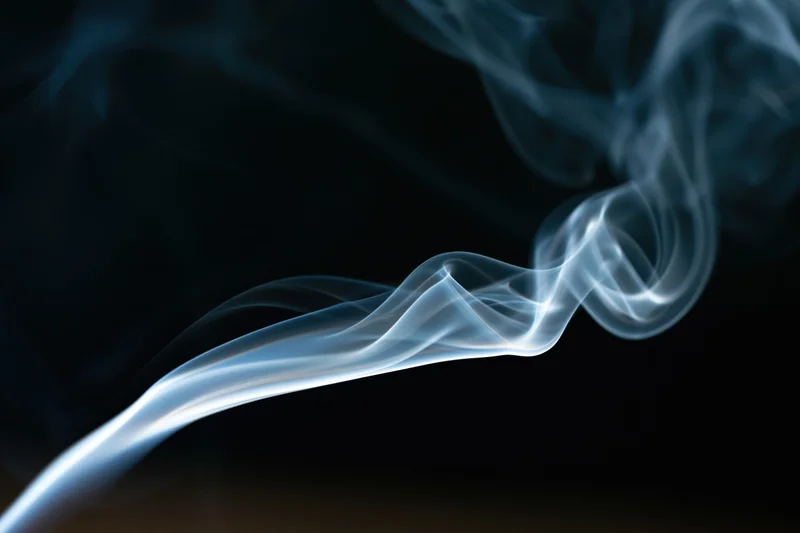 Thin wisp of white-grey smoke curling upward against a dark background