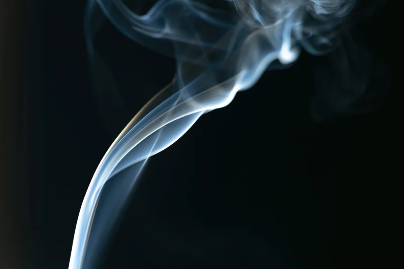 Thin wisp of white-grey smoke curling upward against a dark background