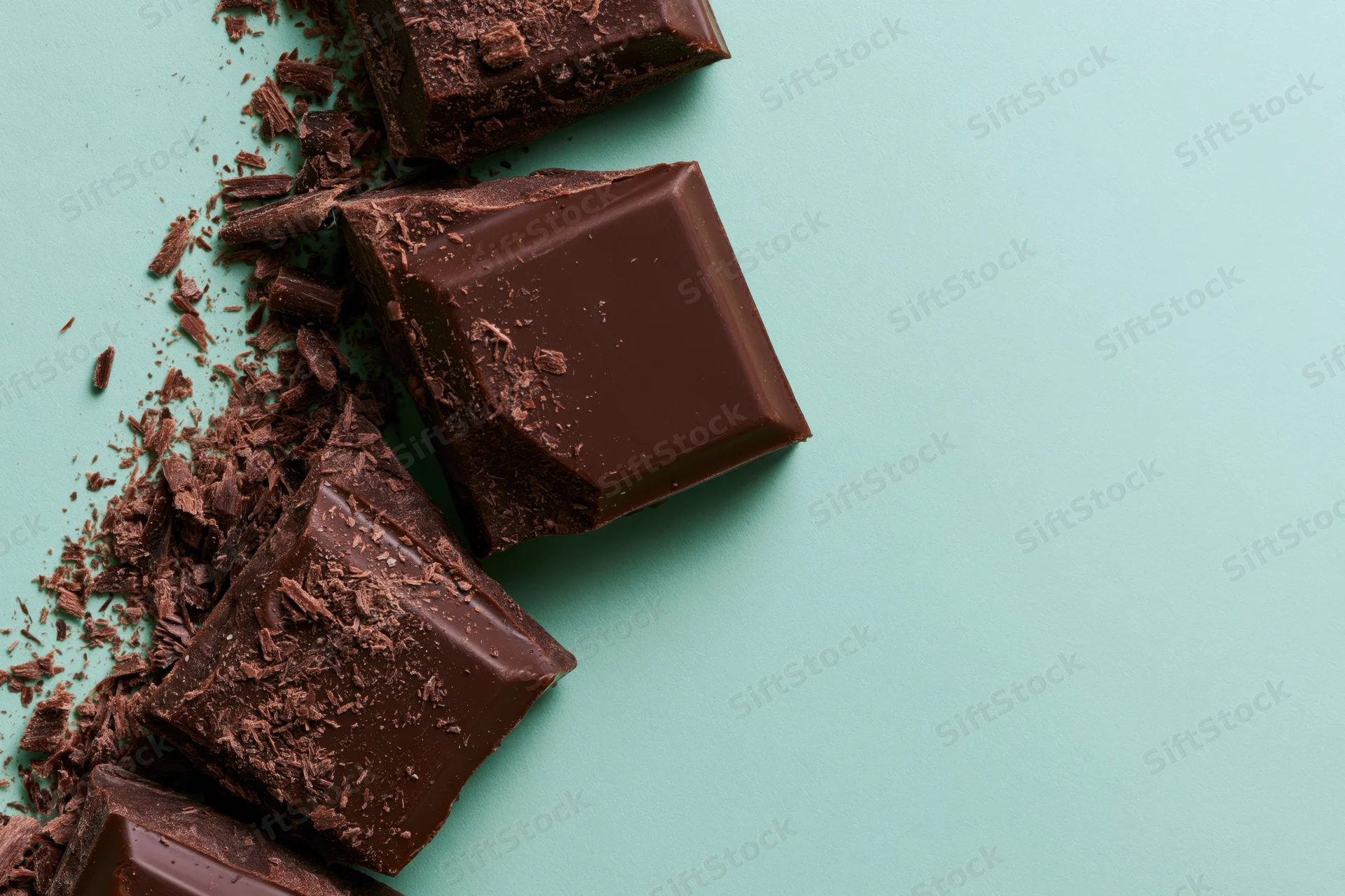 Broken dark chocolate chunks arranged vertically on a teal background with copyspace