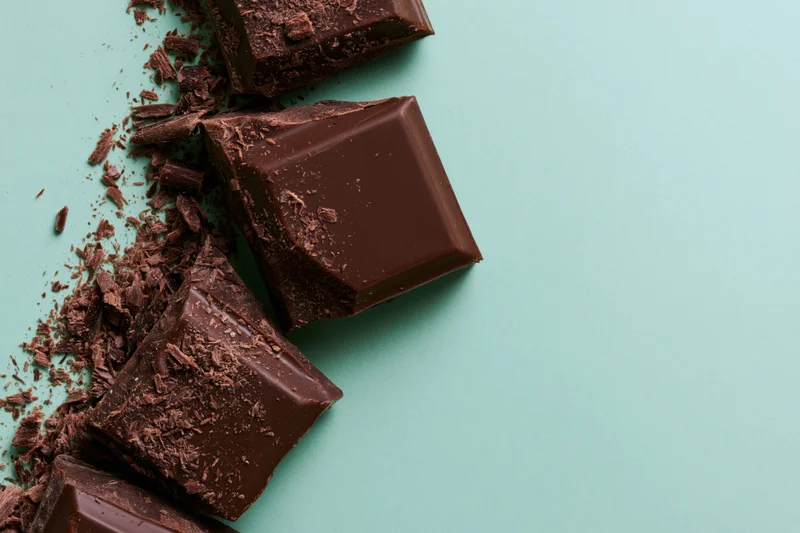 Broken dark chocolate chunks arranged vertically on a teal background with copyspace