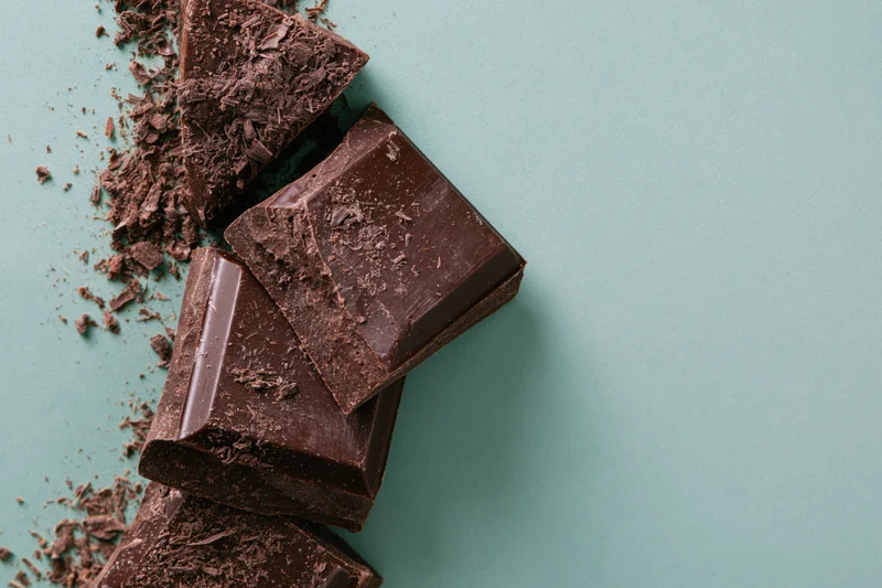Broken dark chocolate chunks arranged vertically on teal background with copyspace