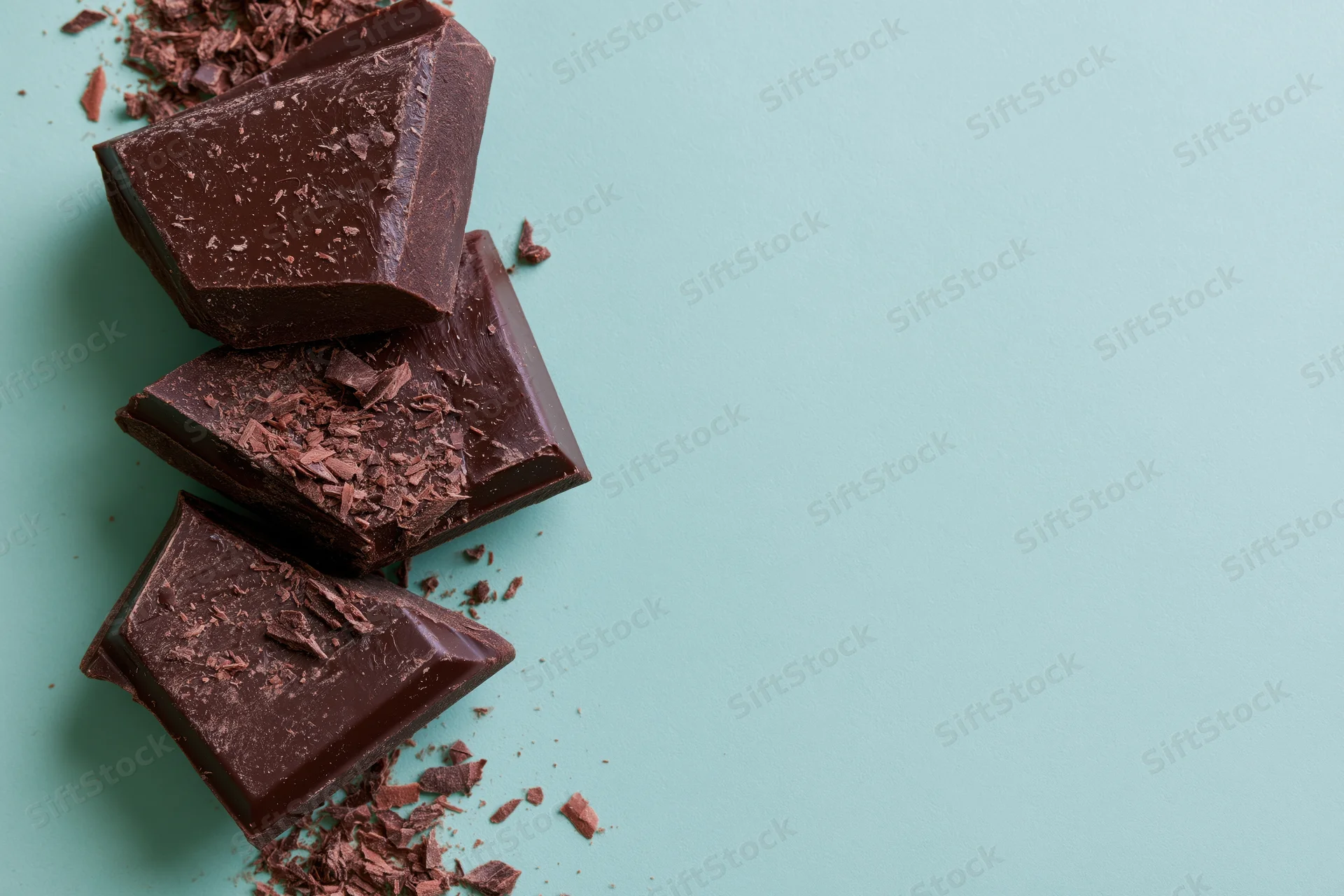 Broken dark chocolate chunks arranged vertically on a mint background with scattered crumbs and copyspace to the right