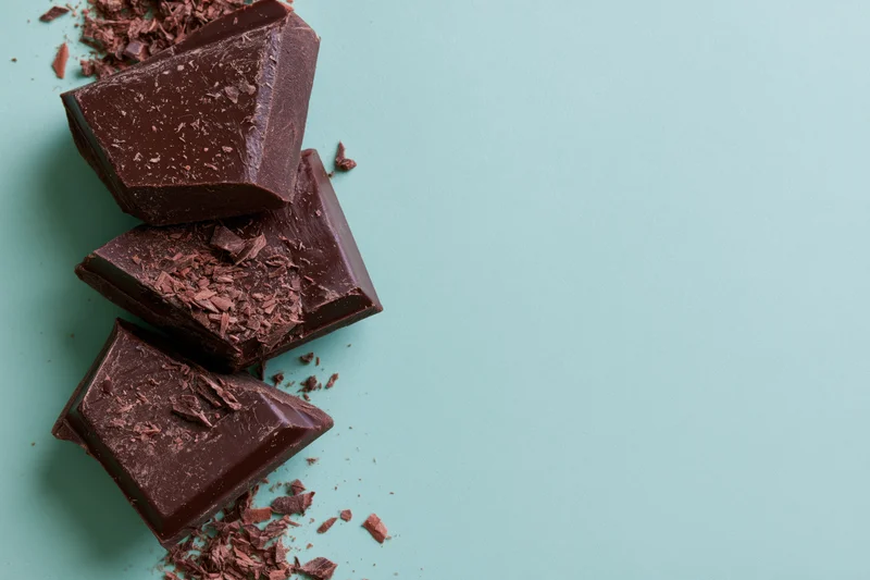 Broken dark chocolate chunks arranged vertically on a mint background with scattered crumbs and copyspace to the right