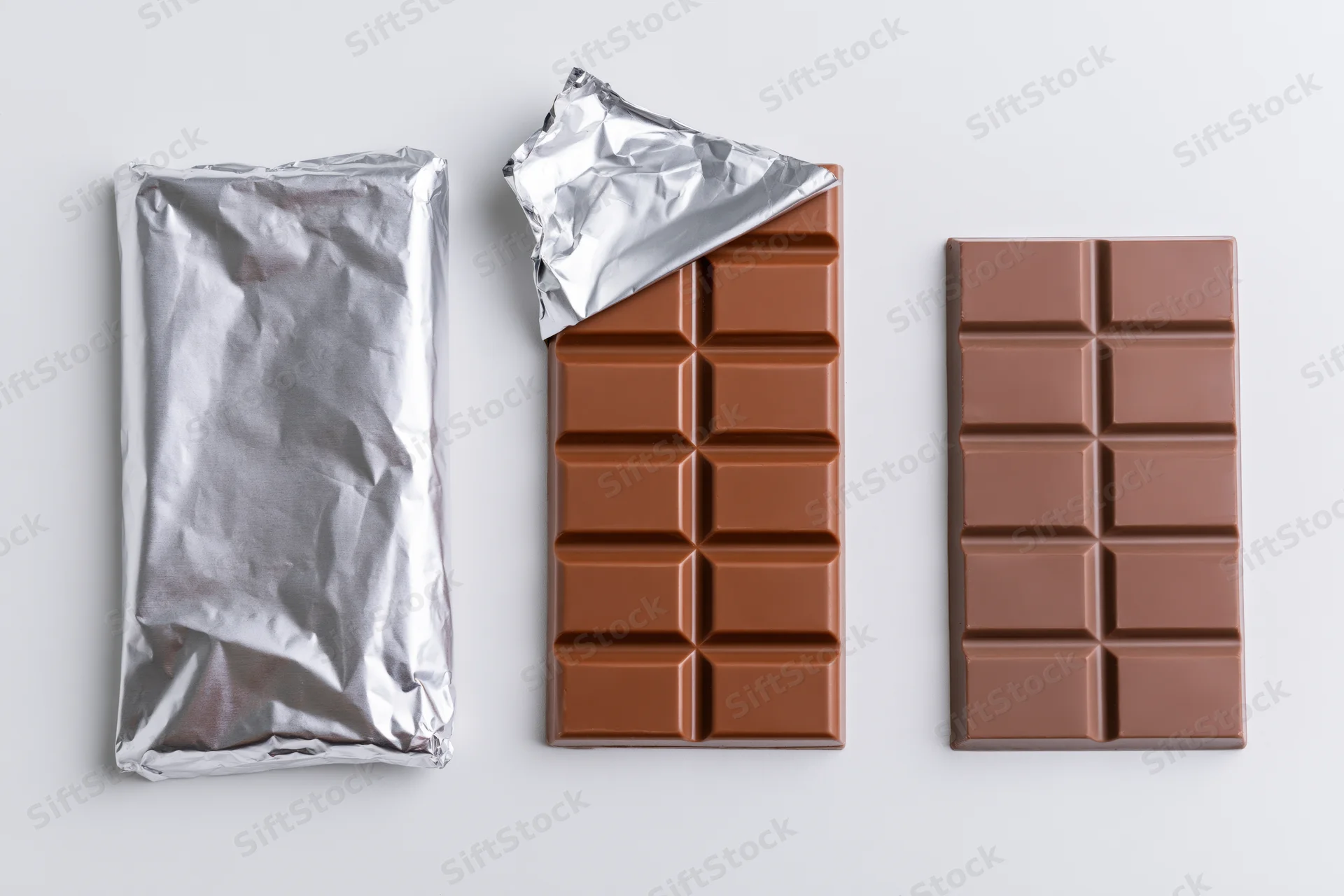 Three milk chocolate bars in a row, one wrapped, one partially unwrapped, one fully unwrapped, on white background