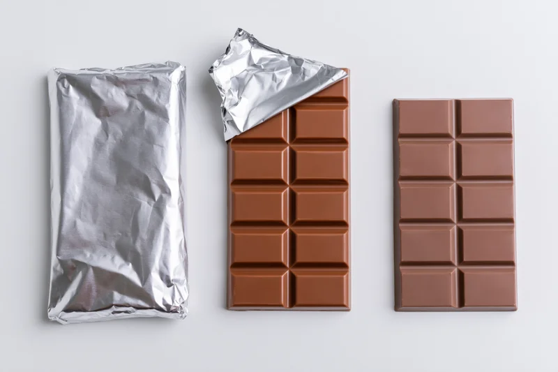 Three milk chocolate bars in a row, one wrapped, one partially unwrapped, one fully unwrapped, on white background