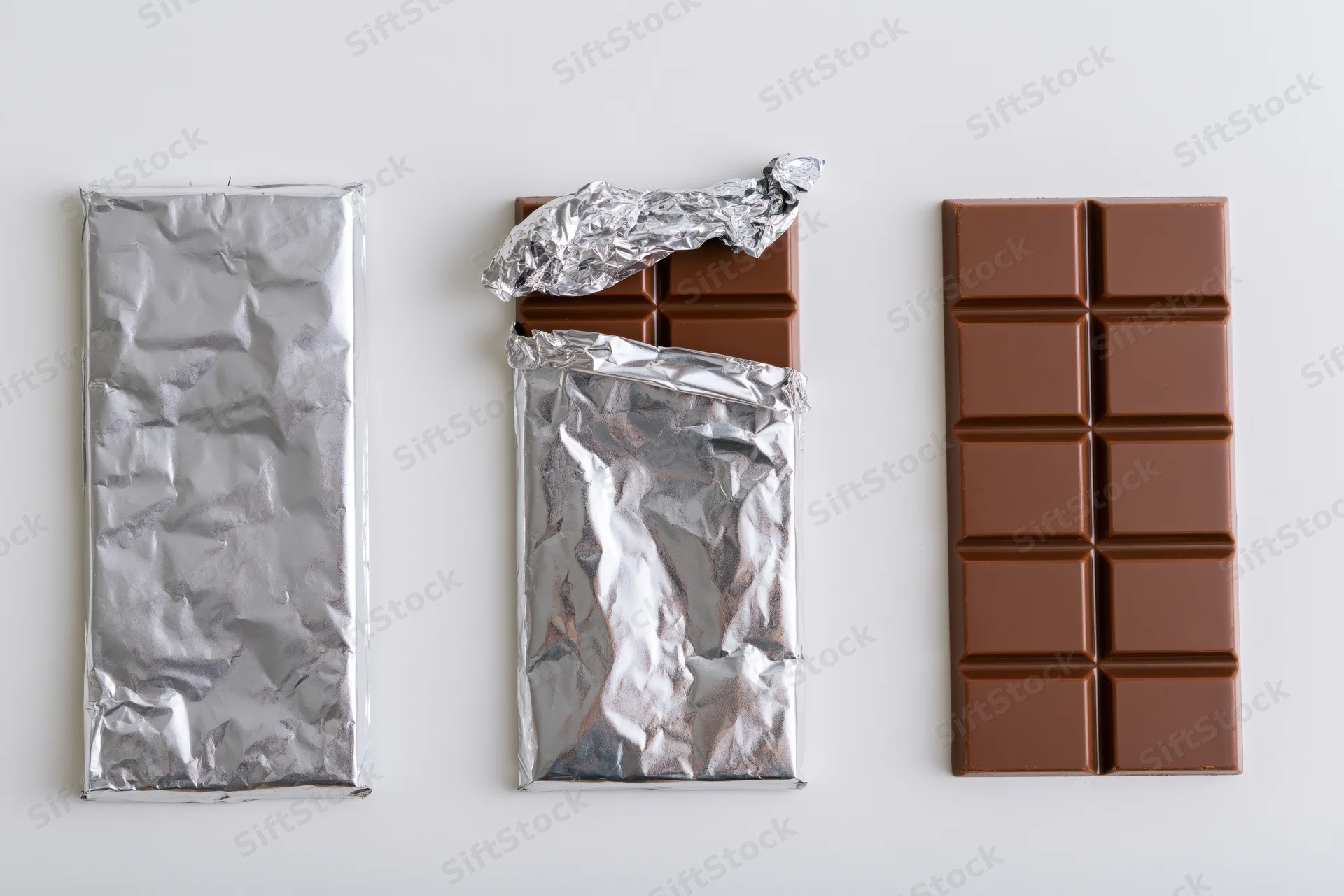 Three milk chocolate bars in varying states of wrapping arranged in a row on a white surface