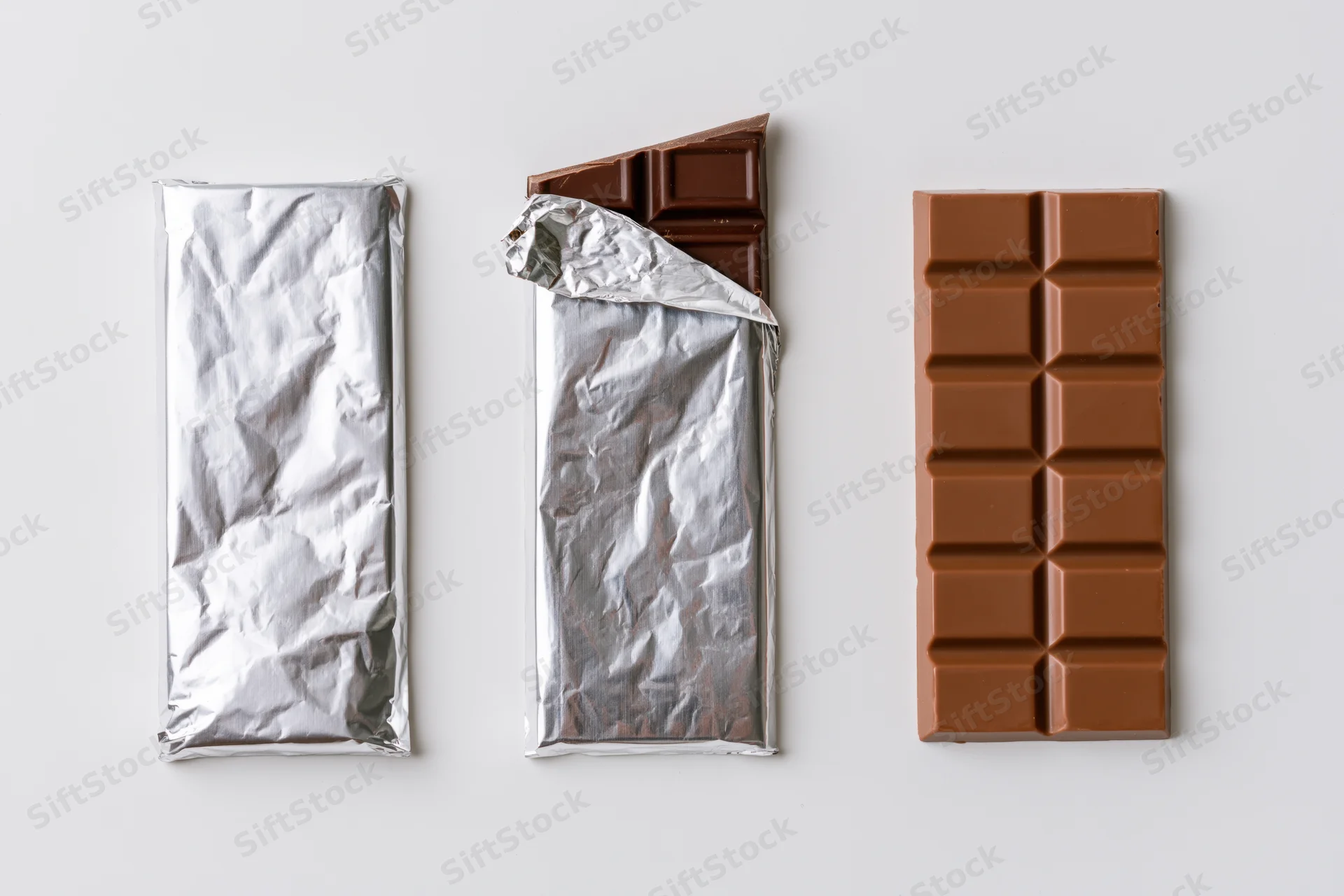 Three milk chocolate bars in wrapped, partially unwrapped, and fully unwrapped states arranged in a row on a white surface