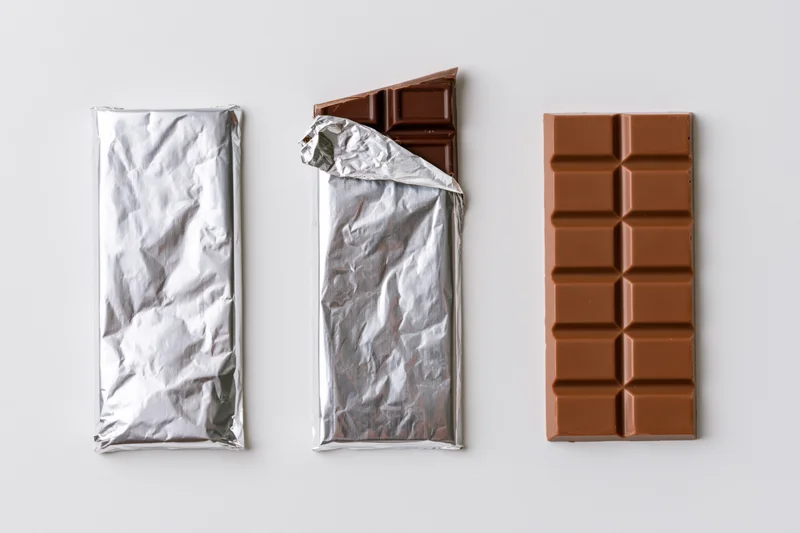 Three milk chocolate bars in wrapped, partially unwrapped, and fully unwrapped states arranged in a row on a white surface