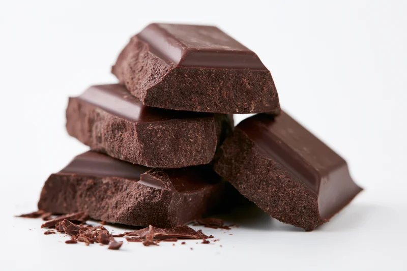 Broken dark chocolate pieces stacked loosely on white background