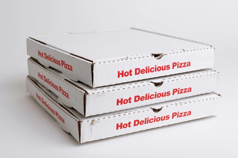 Three stacked white cardboard pizza delivery boxes with red text on a plain white surface