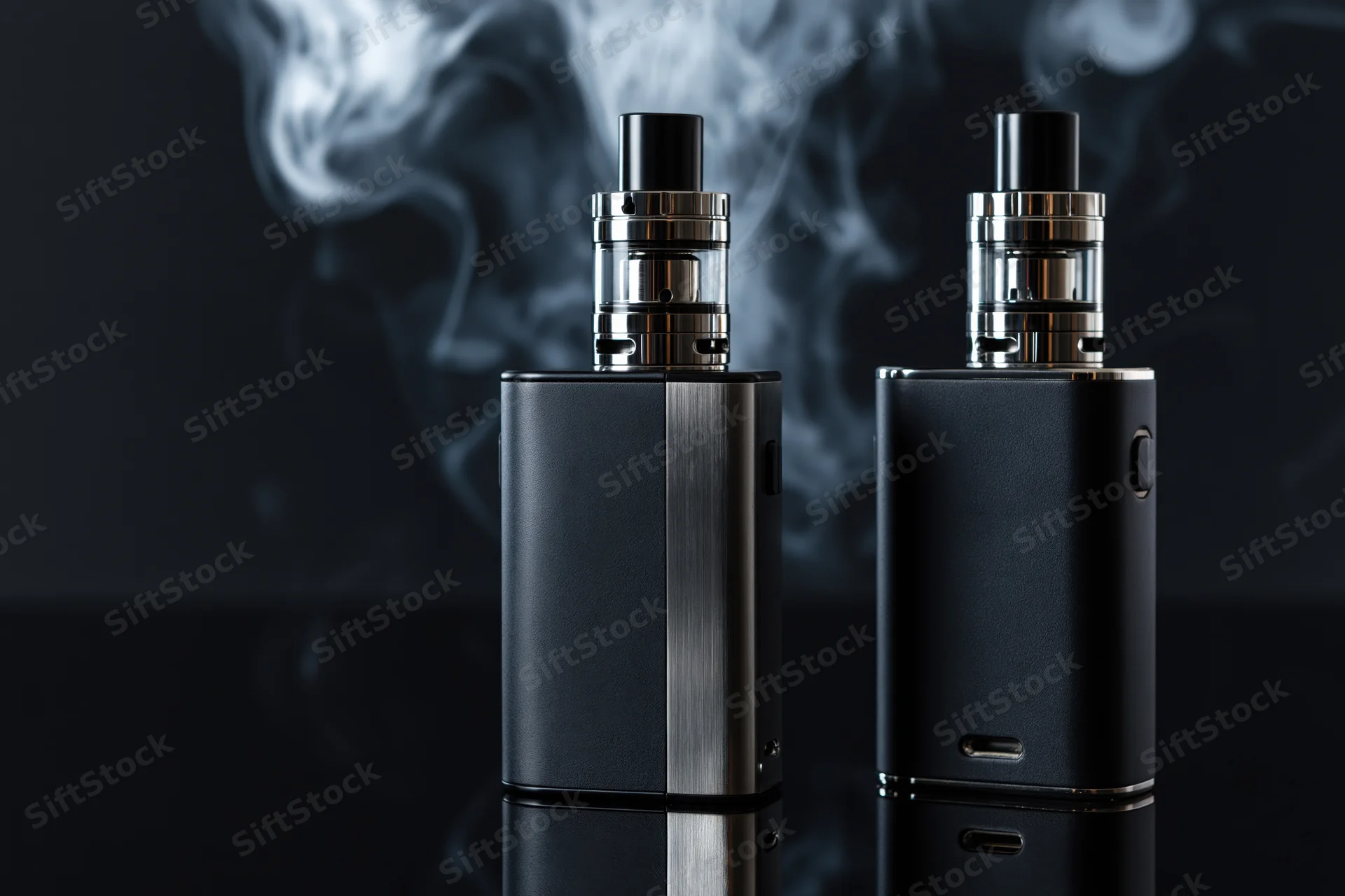 Two black vape mods with chrome atomizers emitting vapor on a dark reflective surface