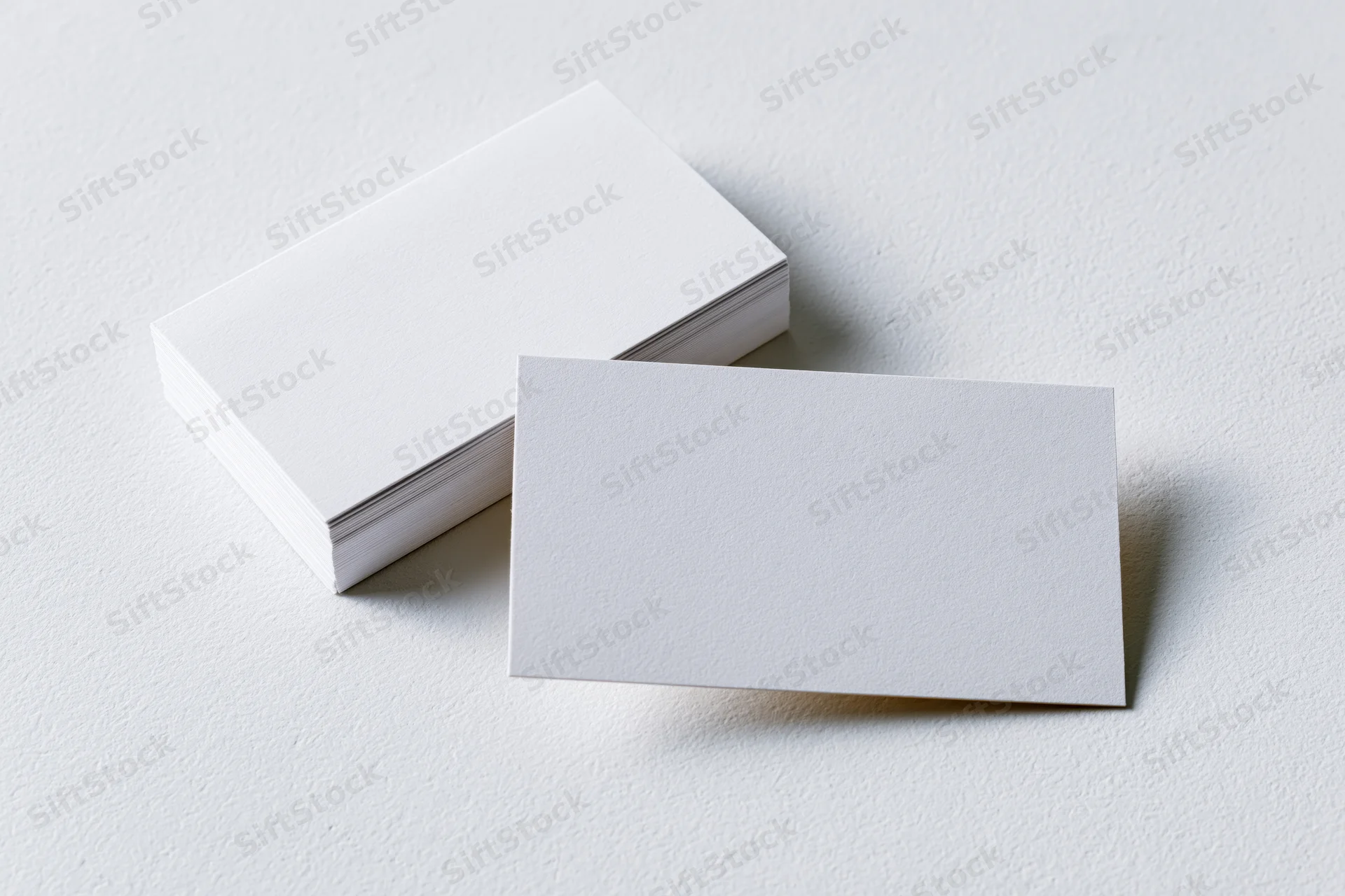 Blank white business cards arranged on textured white surface with one card in front of a stack