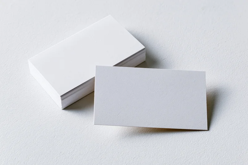 Blank white business cards arranged on textured white surface with one card in front of a stack