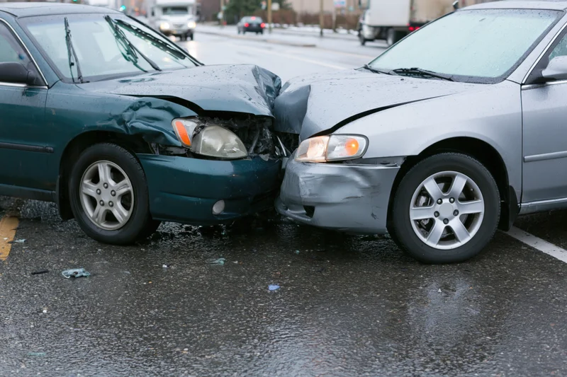 Two damaged cars locked together at front bumpers on wet street