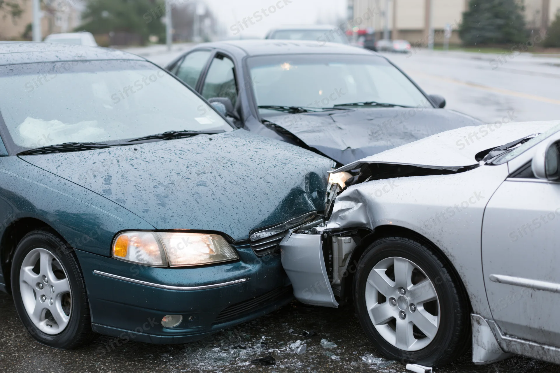 Two damaged cars locked together after a frontal collision on a wet road