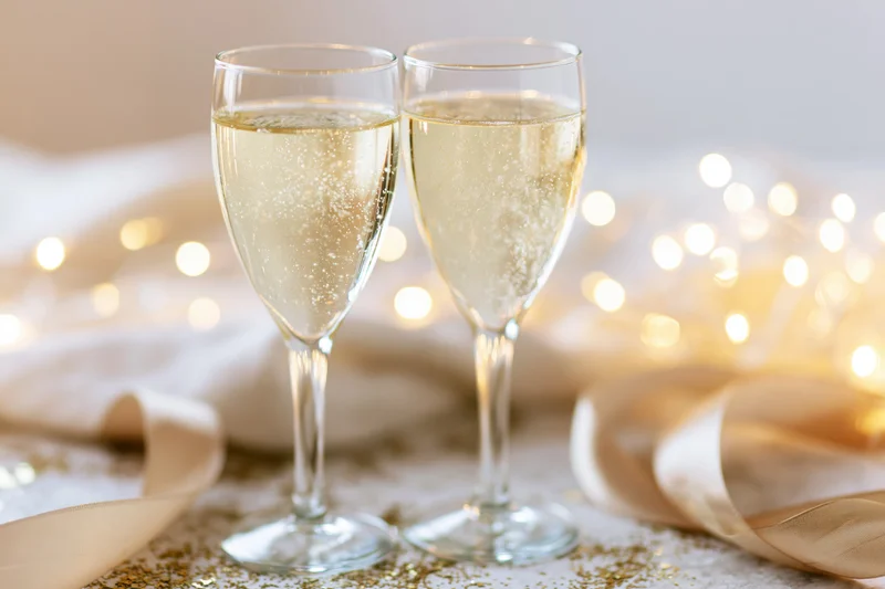 Two champagne flutes filled with sparkling wine on a decorated table with lights and ribbon
