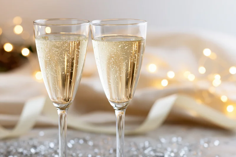 Two champagne flutes filled with sparkling wine on a decorated table with festive lights and silver glitter