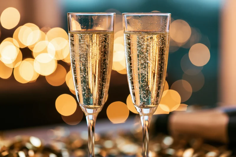 Two champagne flutes filled with sparkling wine bubbles rising against a bokeh light background