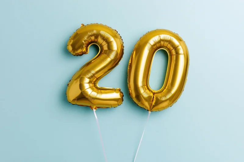Two gold foil number balloons forming 20 floating against blue background