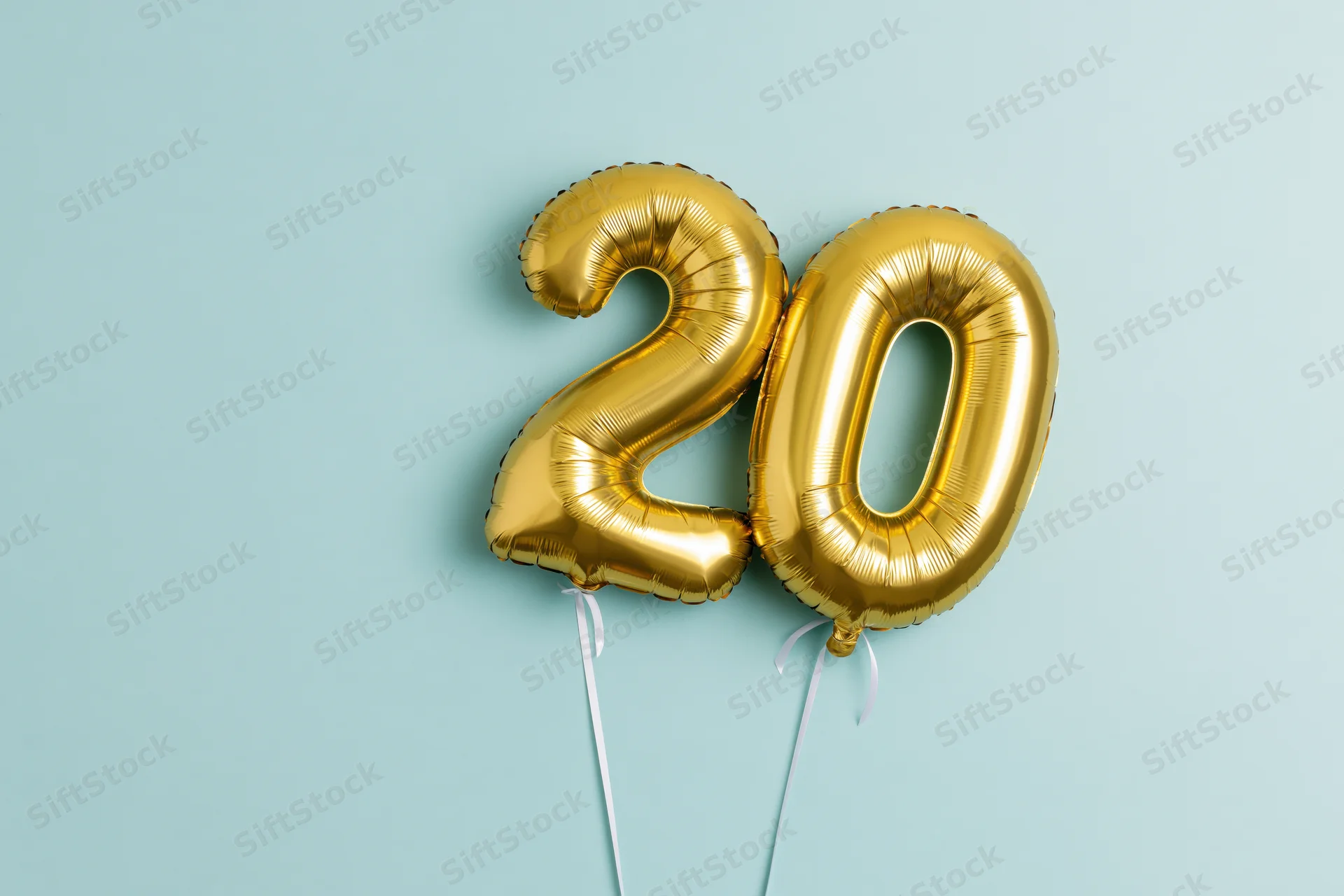 Gold foil number balloons shaped as twenty floating against a light blue background with copyspace