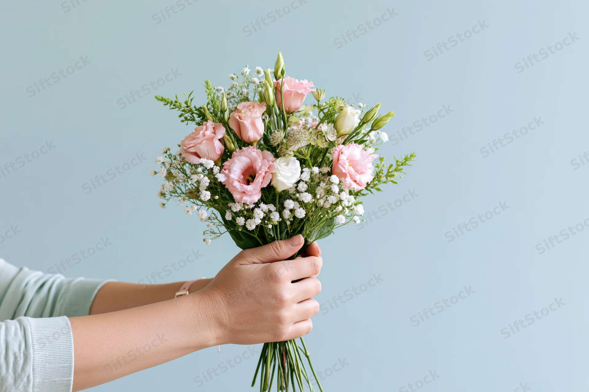 Woman holding a bouquet of pink eustoma and white baby's breath against a light blue background