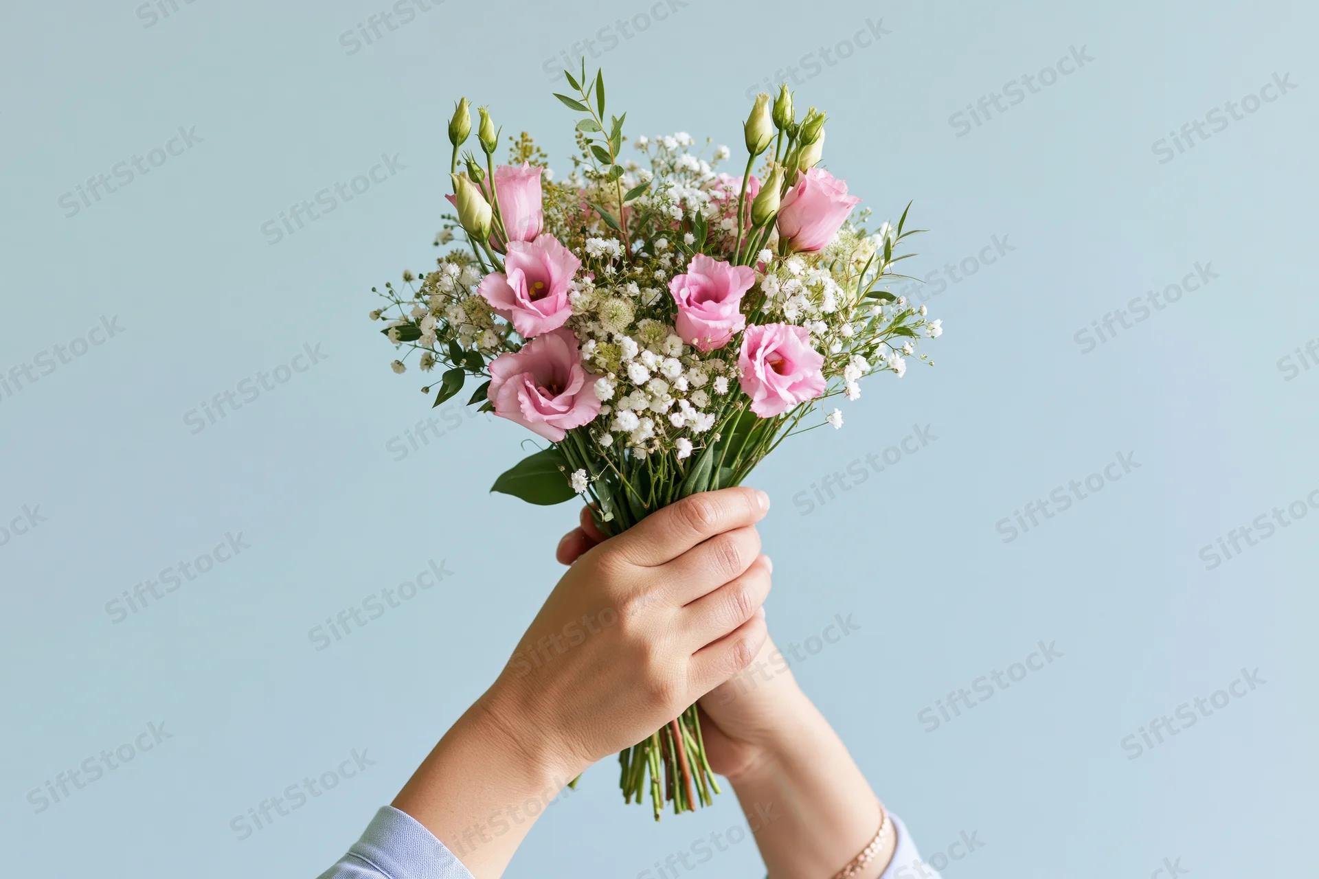 Hands holding a mixed bouquet of pink eustoma and white baby's breath against a light blue background