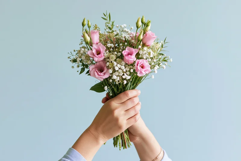 Two hands holding a bouquet of pink eustoma and white flowers