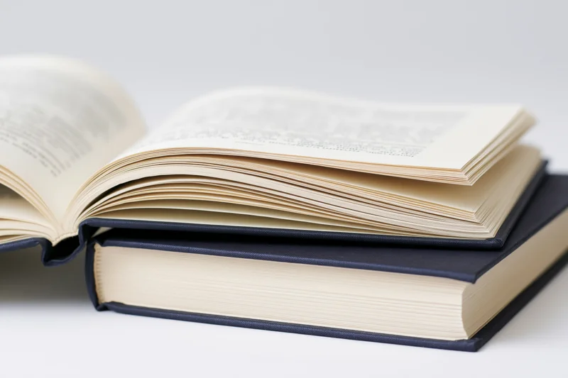 Open hardcover book resting on a closed navy blue book against a white background