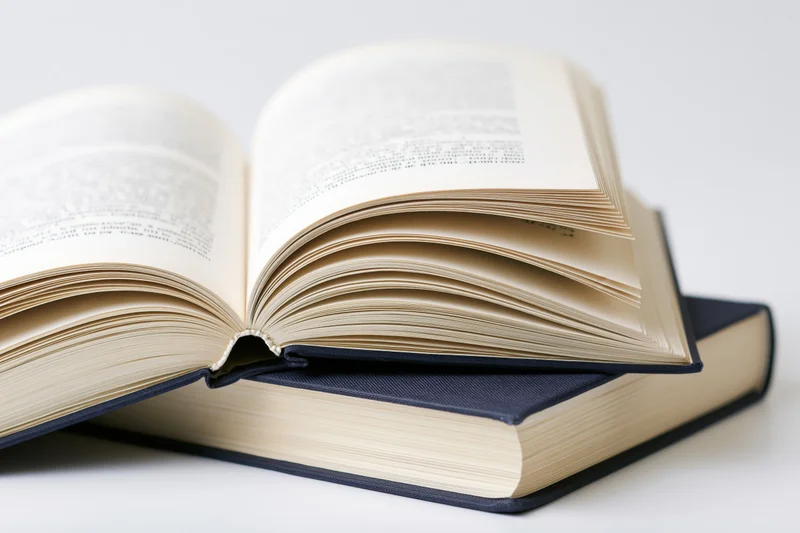 Open hardcover book resting on a closed navy hardcover book against a white background