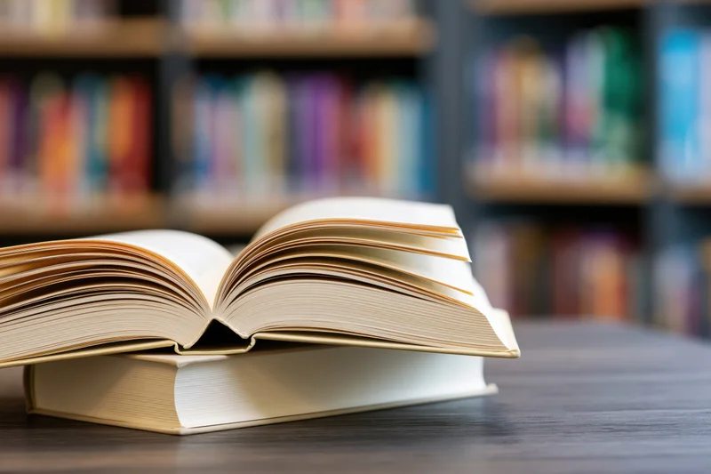 Open hardcover books stacked on a dark wooden table in a library setting