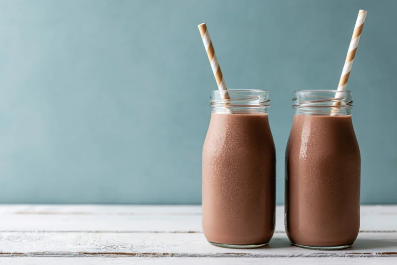 Two glass bottles filled with chocolate milk on a wooden table with striped straws