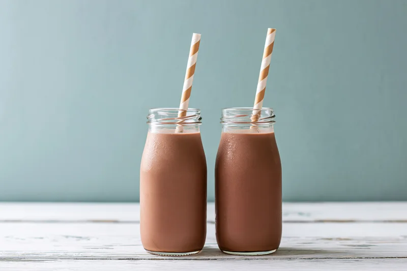 Two glass bottles filled with chocolate milk on a wooden table with striped straws