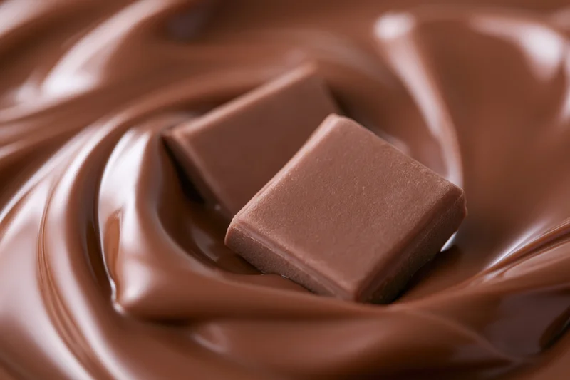 Two milk chocolate squares partially submerged in a swirling pool of melted chocolate