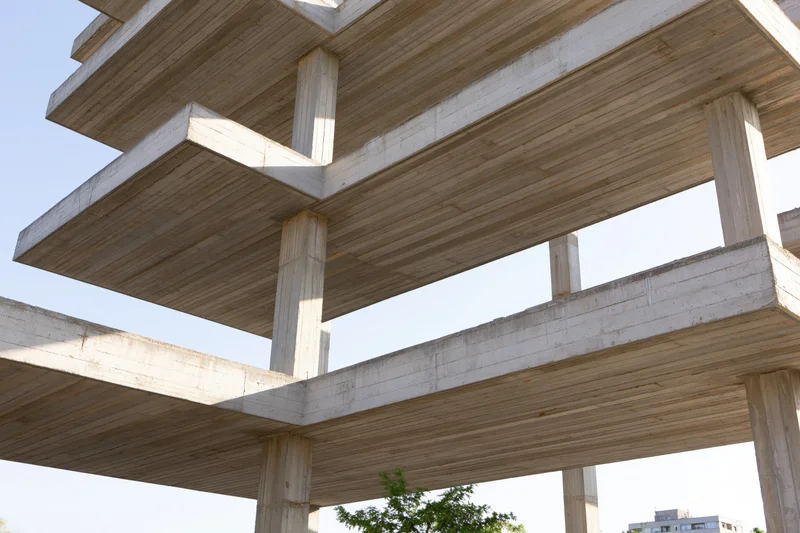 Unfinished brutalist concrete building skeleton with exposed beams and columns under daylight sky