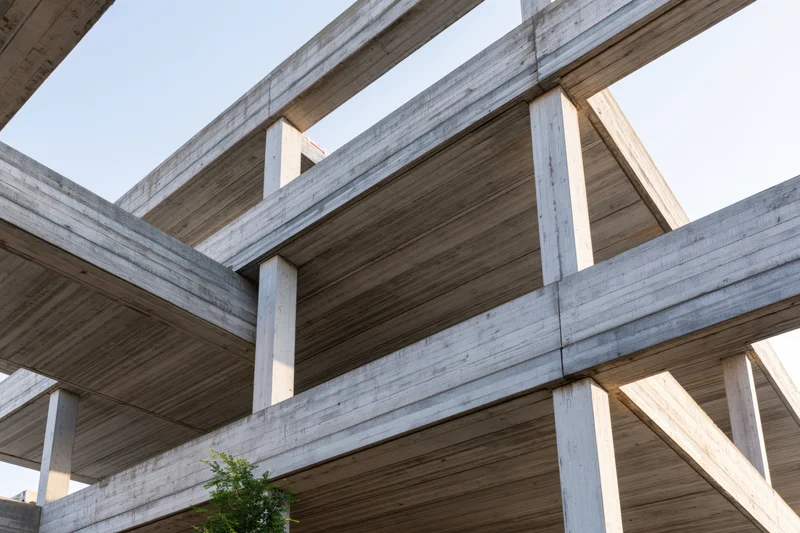 Low-angle view of unfinished brutalist concrete building skeleton with exposed beams and columns under daylight