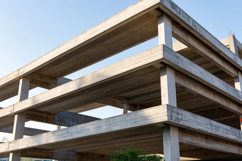 Unfinished brutalist concrete building skeleton with exposed beams and columns under clear sky