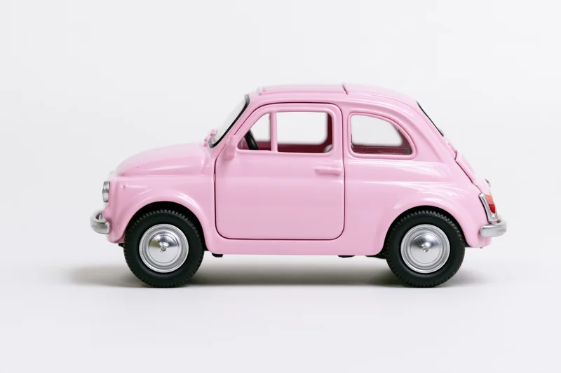 Pink vintage fiat 500 die-cast model car in side profile on white background