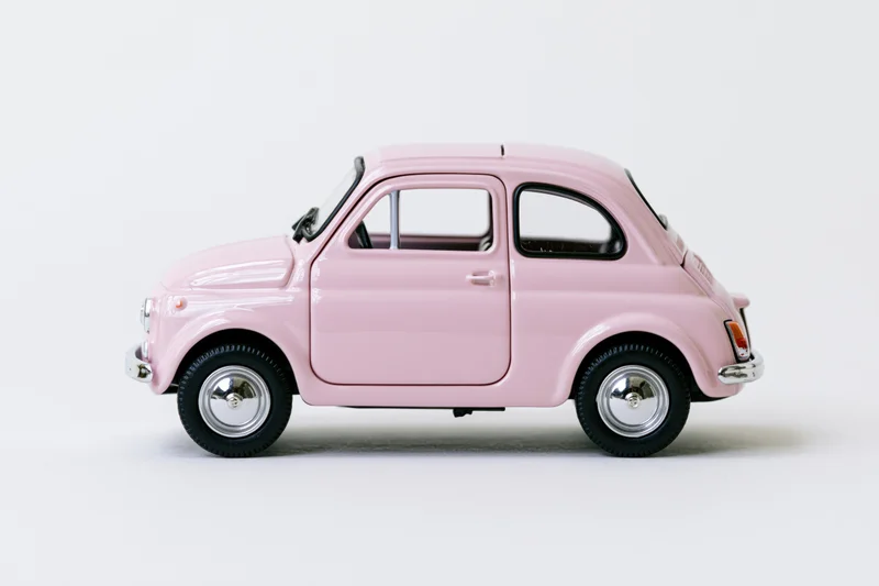 Pink vintage fiat 500 die-cast model car in profile view on white background