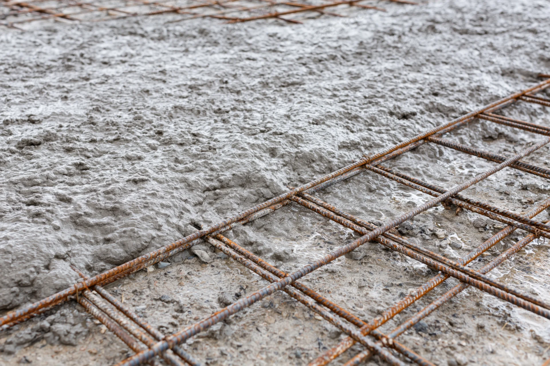 Wet concrete poured over steel rebar grid on a construction foundation
