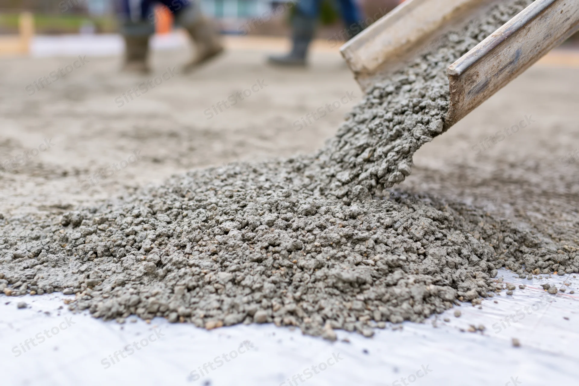Wet concrete pouring from a metal chute onto a flat construction surface