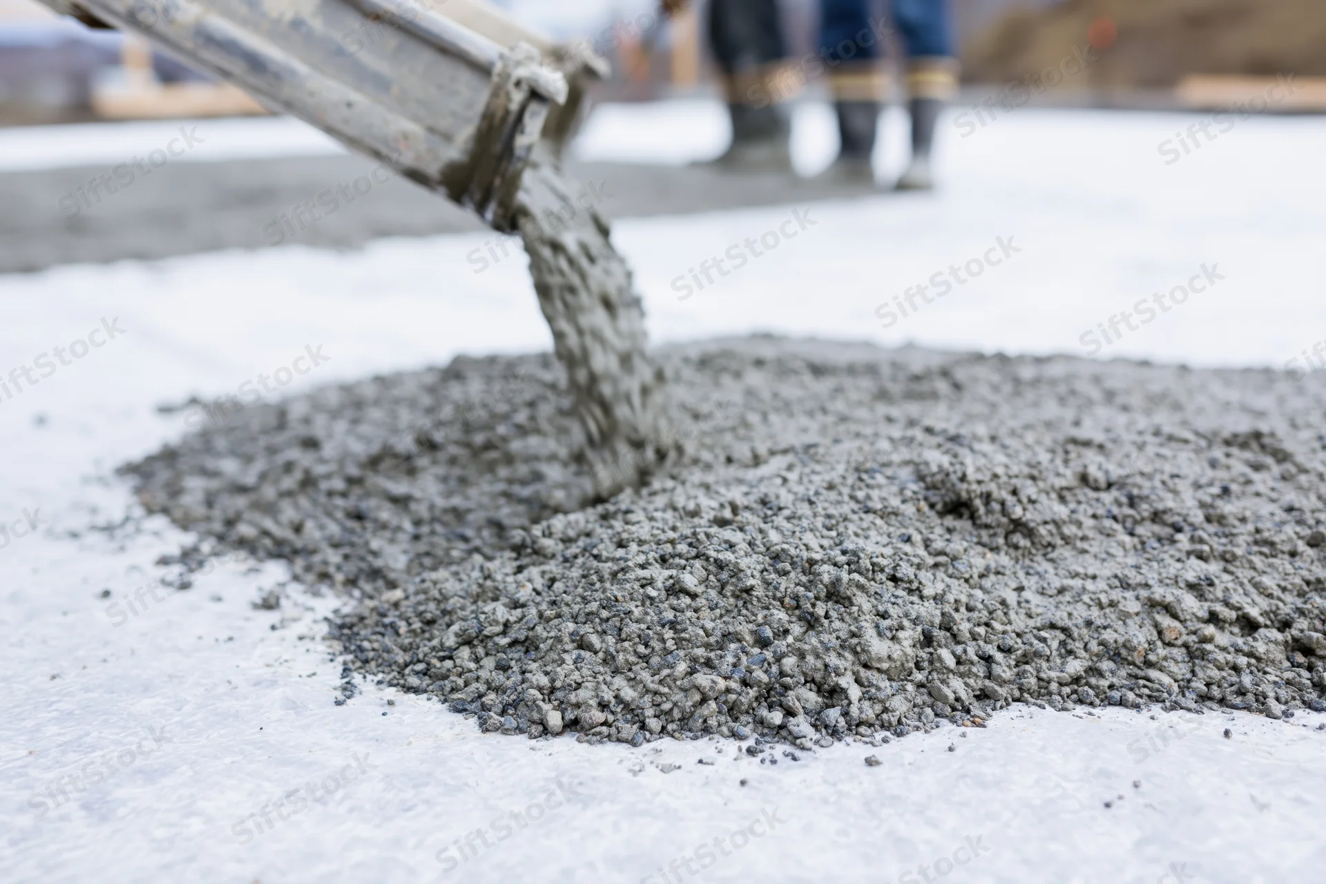 Wet concrete pouring from a metal chute onto a snowy construction site