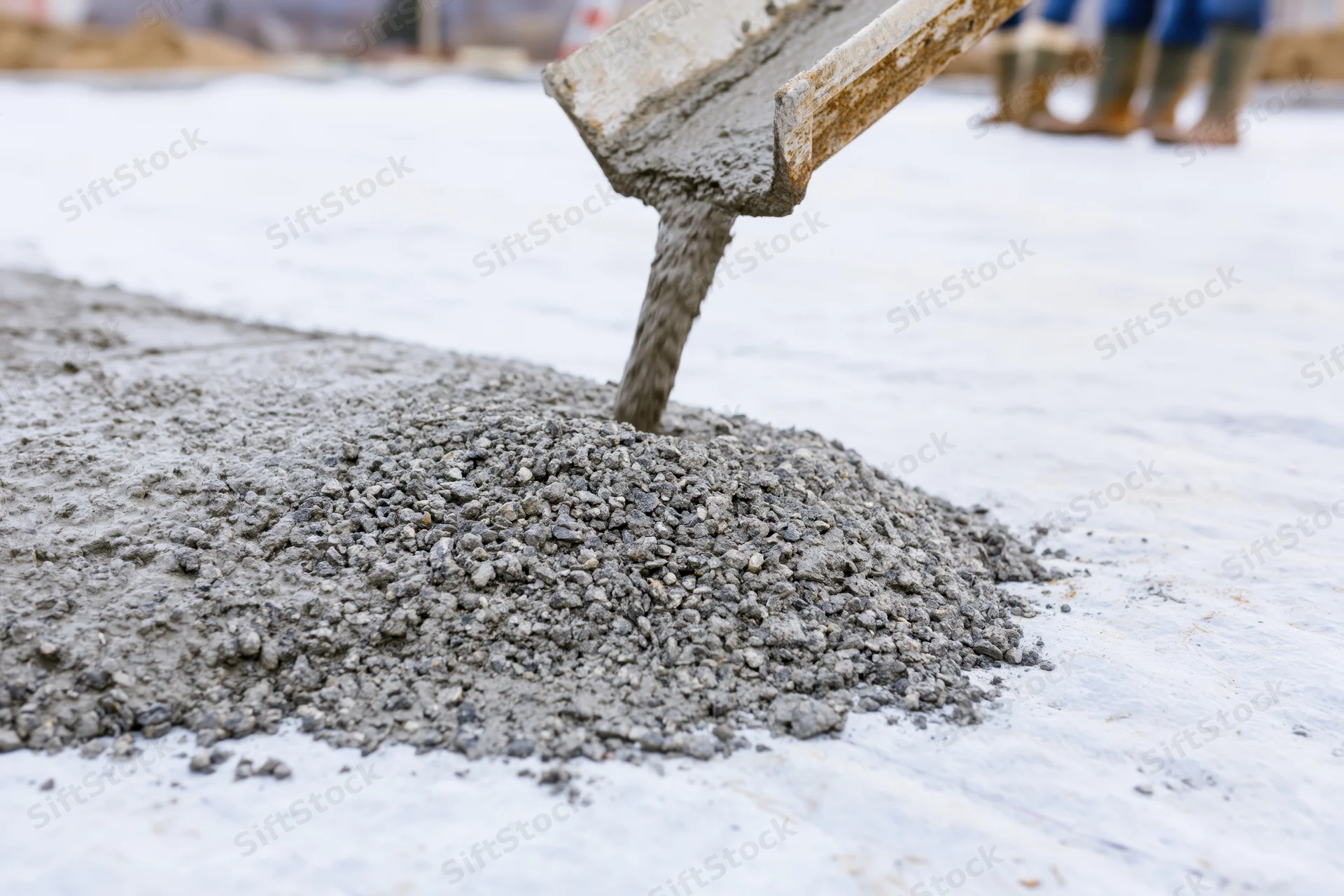 Wet concrete pouring from a metal chute onto a flat construction surface