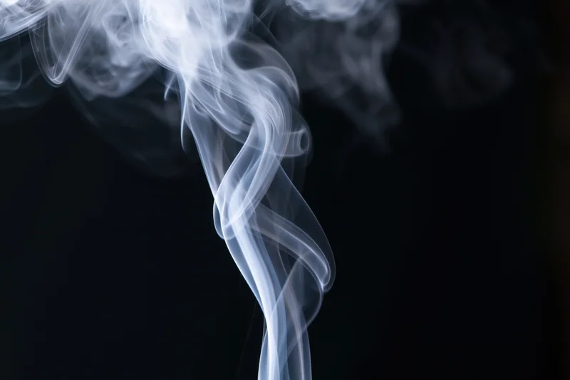 White smoke rising in delicate curls against a dark background
