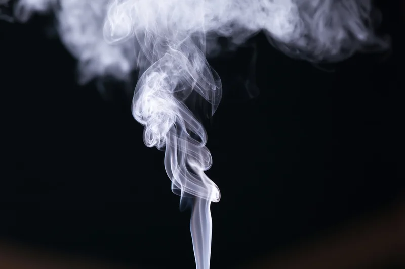 White smoke rising and curling upward against a black background