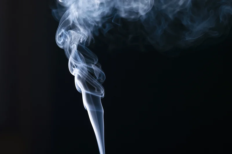 White smoke rising in delicate curls against a black background