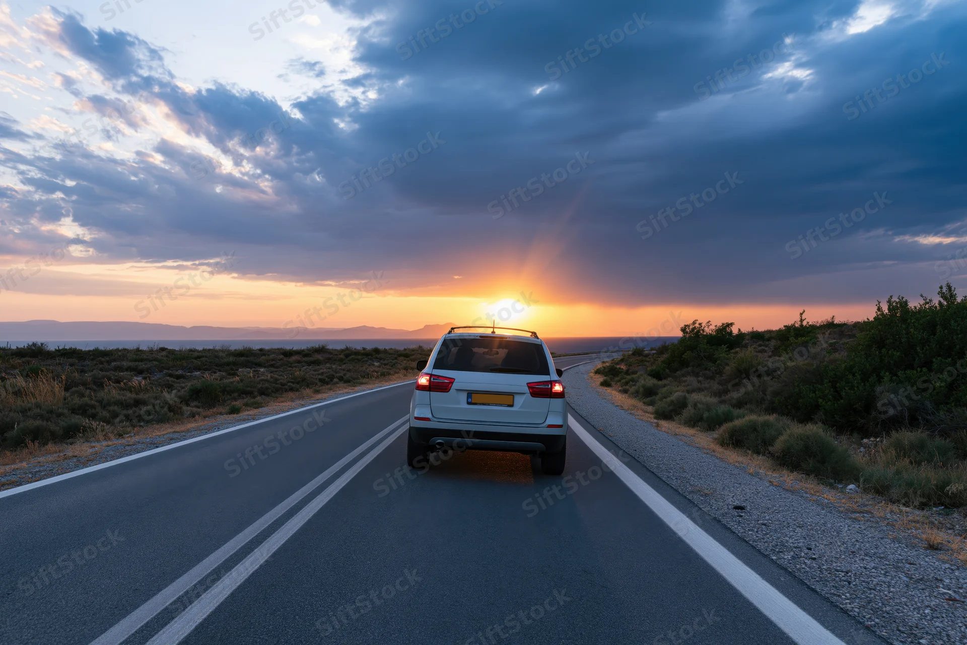 White suv driving away on a coastal highway at sunset